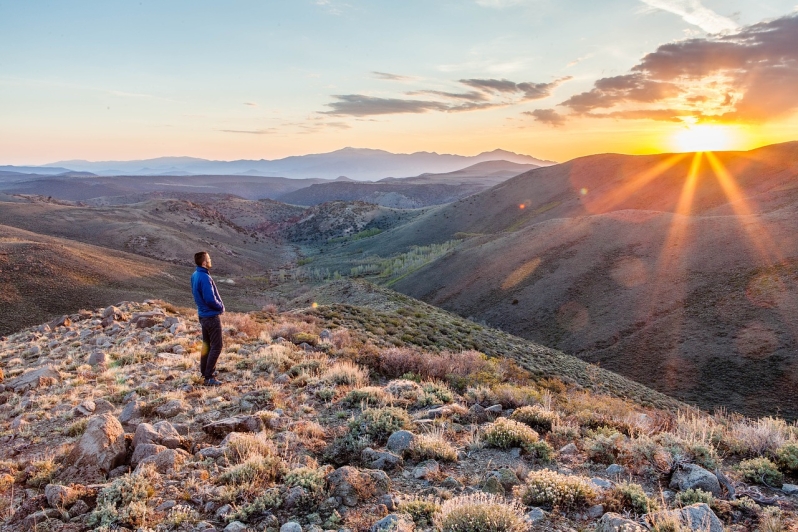 Une personne debout sur une colline, seule, au coucher du soleil.